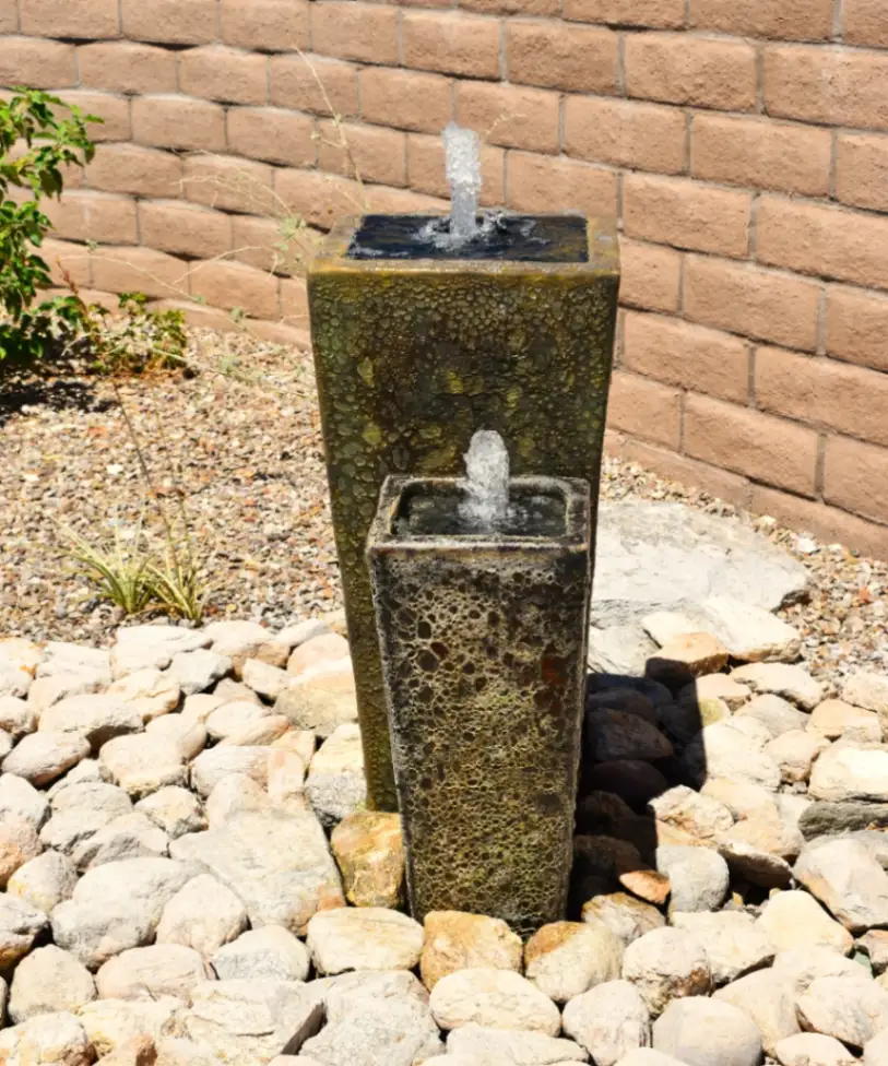 A Sculptural Twin Column Fountain By Sonoran Gardens Inc., With Bubbling Water Over Glazed Ceramic Surfaces, Nestled In River Rock For A Tranquil Desert Accent