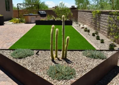 Contemporary Tucson Backyard With Triangle Shaped Steel Planter, Totem Cactus, Artificial Turf Lawn, Outdoor Grill Area, And Gravel Beds With Low Water Plant
