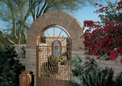 Elegant Garden Entrance Featuring Brick Arch Iron Gate And Blooming Plants