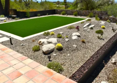 Gravel Mulched Xeriscape With Golden Barrel Cactus, Desert Succulents, Boulders, And A Rectangular Artificial Turf Lawn Bordered By Stone And Tile In A Tucson Backyard