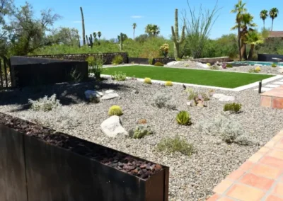 Modern Desert Yard With Gravel Mulch, Golden Barrel Cactus, Ornamental Succulents, Rusted Steel Planter Walls, And Artificial Turf Bordered By Terra Cotta Tile In Tucson