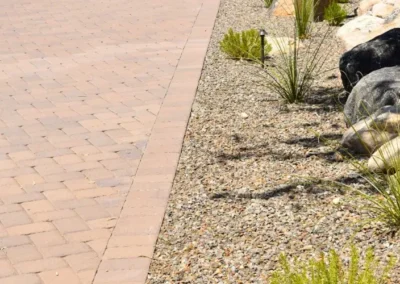 Tucson Front Yard With Gravel Mulch, Low Water Desert Plants, Modern Landscape Lighting, Natural Boulders, And A Paver Driveway Leading To A Southwestern Style Home