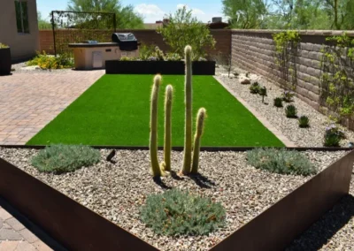 Backyard desert landscaping with artificial turf, cactus, gravel, and outdoor patio area