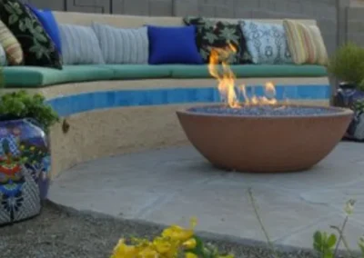 A curved stone bench with colorful cushions and a round fire pit on a stone patio