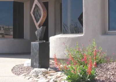 Modern abstract metal sculpture standing in a desert home garden with red flowers