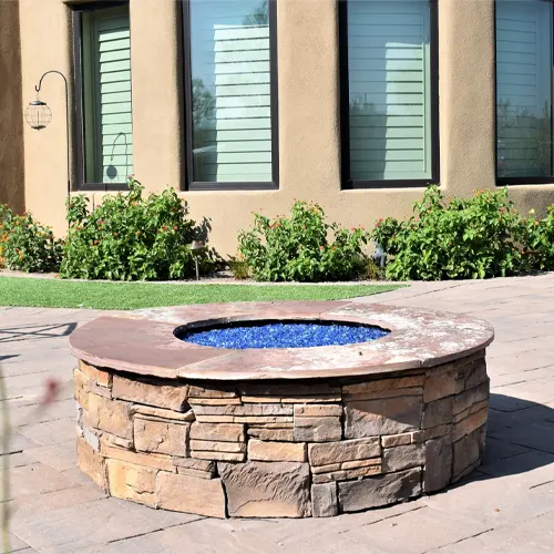 Stone fire pit with blue glass on a backyard patio in front of a house