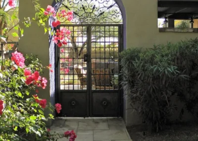 Decorative wrought iron gate entrance framed by vibrant pink bougainvillea flowers in a courtyard