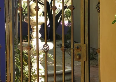 A view through a decorative wrought iron gate into a courtyard with a stone water fountain