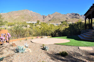 Tucson backyard with circular flagstone patio, artificial turf, agave, prickly pear cactus, gravel mulch, and mountain views in the background.